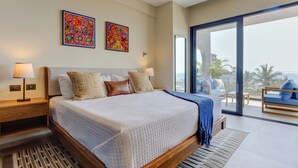 A modern bedroom with a large bed, two wall art pieces, a balcony with a view, and a wooden nightstand with a lamp.