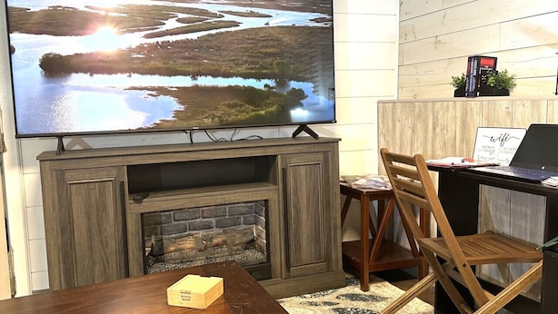 Una sala de estar con televisión, chimenea, muebles de madera y una computadora portátil sobre un escritorio.