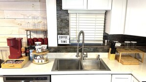 Una cocina con un lavamanos de acero inoxidable, una cafetera y una estación de café con tazas y tarros.