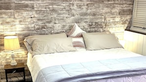 Una cama con colcha acolchada, dos almohadas, una lámpara de noche y un cabecero de madera.