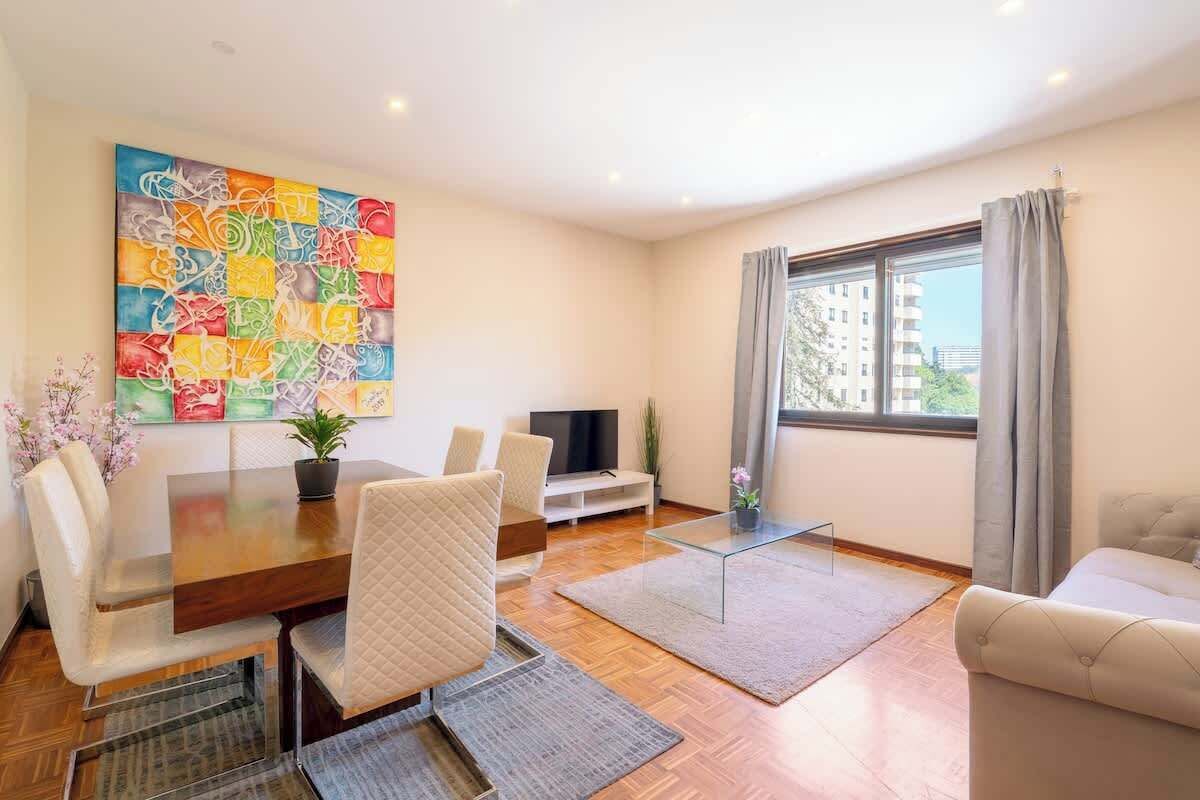 Un salon moderne avec une table à manger en bois, des chaises de couleur beige, une table basse en verre et un grand tableau abstrait accroché au mur.