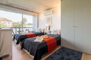 A modern hotel room with two beds, a desk, a chair, and a large window. - Apartment with balcony and pool by Hostwise (Vila Nova de Gaia)