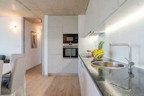 A modern kitchen with a built-in oven, a stainless steel sink, and a fruit bowl on the counter. - Apartment with balcony and pool by Hostwise (Vila Nova de Gaia)