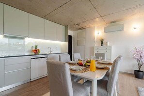 Una cocina moderna con armarios blancos, una mesa de comedor para cuatro personas y una planta en maceta a la derecha.