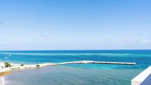 Vista costera con muelle que se adentra en el mar, cielos despejados y una costa distante.