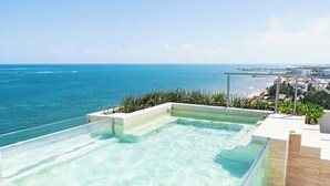 Una piscina infinita en la azotea con vistas al océano y un horizonte urbano distante.