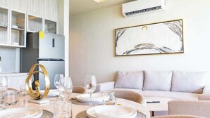 Una sala moderna con un sofá, una mesa de comedor preparada para una comida y una cocina con armarios y aire acondicionado.