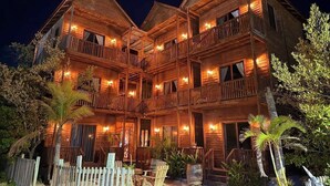A multi-story wooden building with balconies, a wooden fence, and tropical plants.
