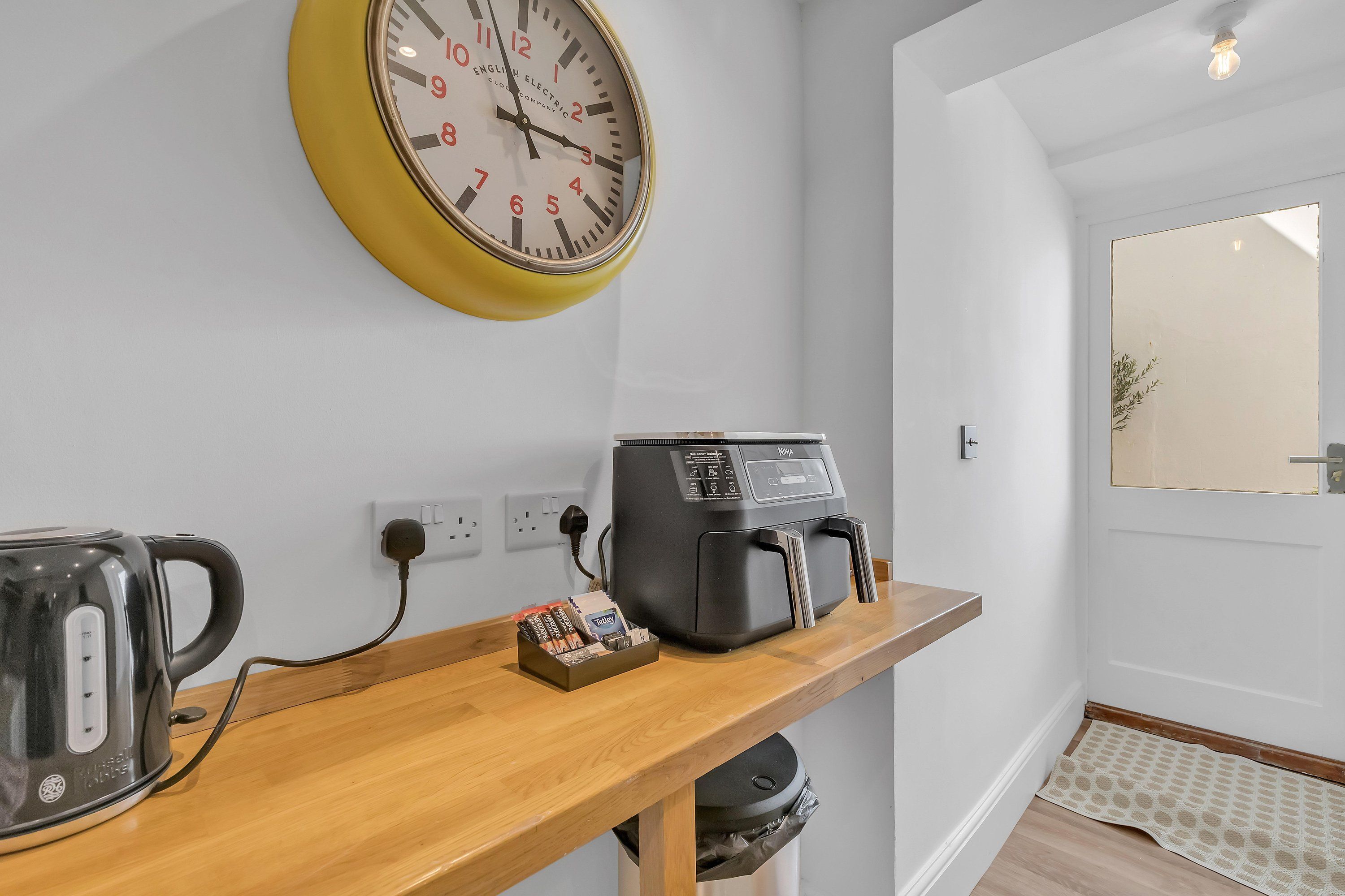 A kitchen area with a kettle, coffee maker, and a clock on the wall.