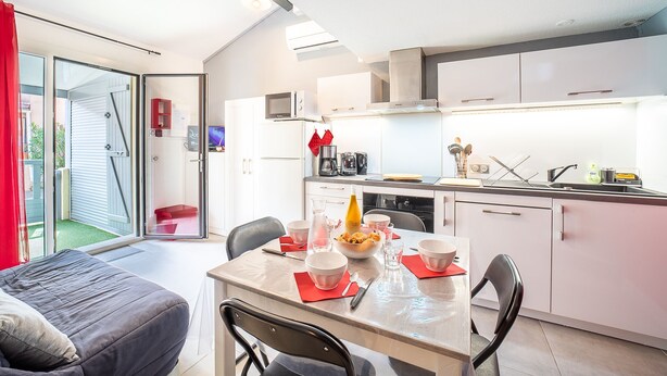 A modern kitchen with white cabinets, a microwave, and a coffee maker. There is a dining table with red placemats and bowls. - Notre Patio - Maisonette climatisée proche plage (Saint-Cyprien)