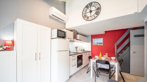 A compact kitchen with white cabinets, a microwave, and a clock on the wall. - Notre Patio - Maisonette climatisée proche plage (Saint-Cyprien)