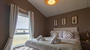 Ein Schlafzimmer mit großem Fenster, einem Bett mit weißer Bettwäsche, einer Bank und Wandbildern.