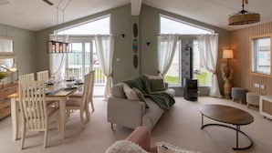 Ein großzügiger Wohnbereich mit Esstisch, Stühlen, einer Couch und einem Couchtisch. Ein Kamin, ein Deckenventilator und große Fenster mit Vorhängen sind ebenfalls vorhanden.