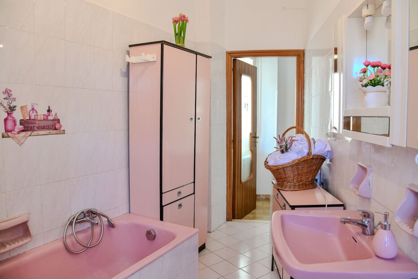 Un bagno con due lavandini rosa, una vasca, un armadietto e uno specchio.