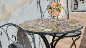 Un juego de mesa y sillas de metal con un tablero de mosaico de colores, situado en un patio con baldosas.