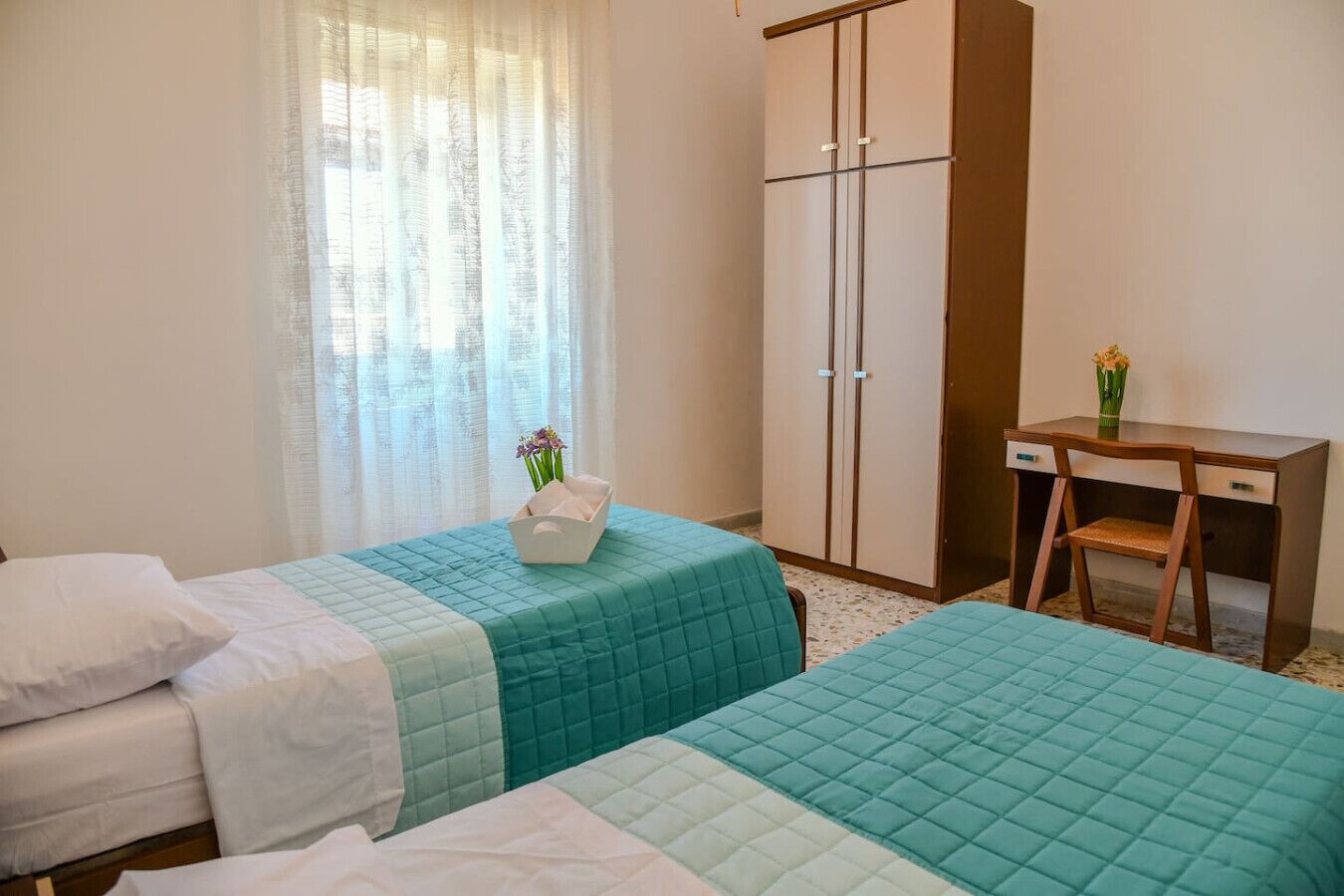 A hotel room with two beds, a desk, and a wardrobe.