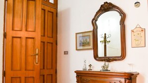 Una habitación con puerta de madera, un espejo sobre un tocador de madera y suelo de baldosas.