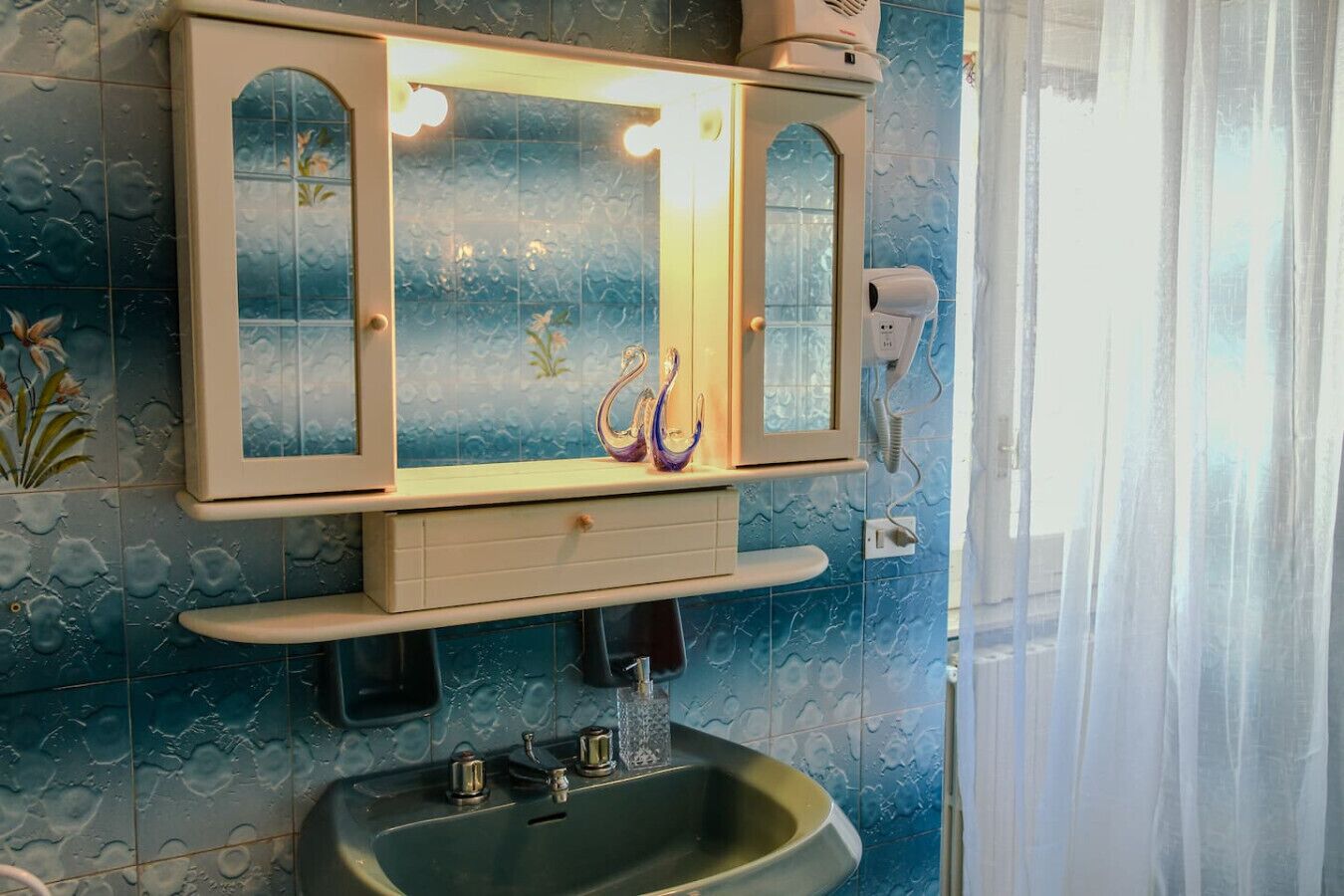 Une salle de bain avec un grand miroir, un lavabo et un sèche-cheveux fixé au mur.
