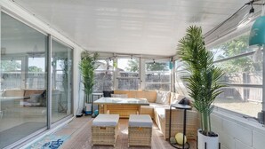 A covered patio with a glass door, wicker furniture, and potted plants.
