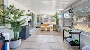 A covered patio area with a seating area, potted plants, and a fan.