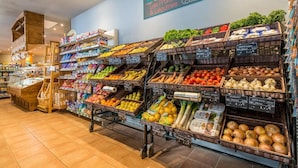Un supermercado con diversas frutas y verduras a la vista, incluyendo cestas de manzanas, naranjas y tomates.