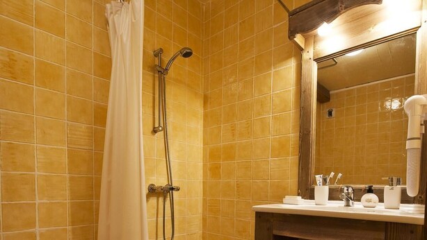 Un bagno con doccia, lavandino e pareti rivestite di piastrelle.