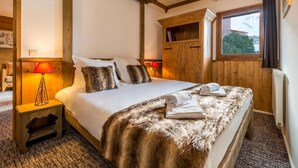 Un dormitorio con una cama grande, cabecera de madera y ventana con vistas a árboles. Hay dos mesitas de noche con lámparas y un armario.