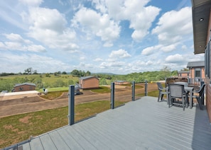 Um terraço com área de estar externa, vista para o campo e um pequeno edifício ao fundo.