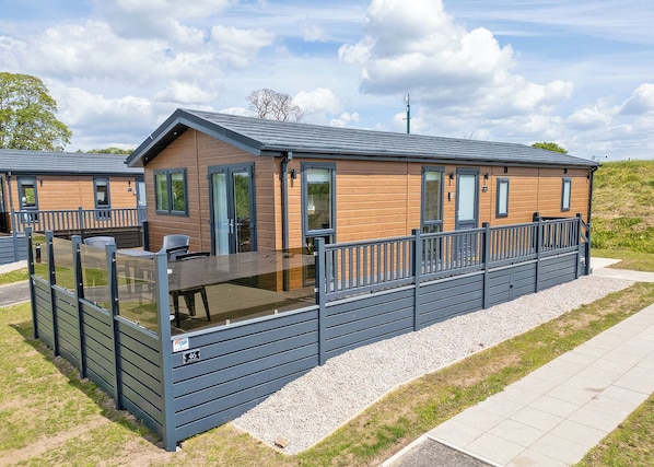 Eine moderne Hütte mit einer Terrasse, großen Fenstern und einem Kiesweg.