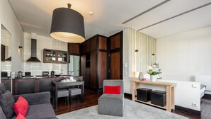 A modern living room with a grey sofa, a red pillow, and a grey ottoman. There is a dining area with a table and chairs, and a kitchen with a stove and cabinets. - Charming Apartment with street-view in Porto (Oporto)
