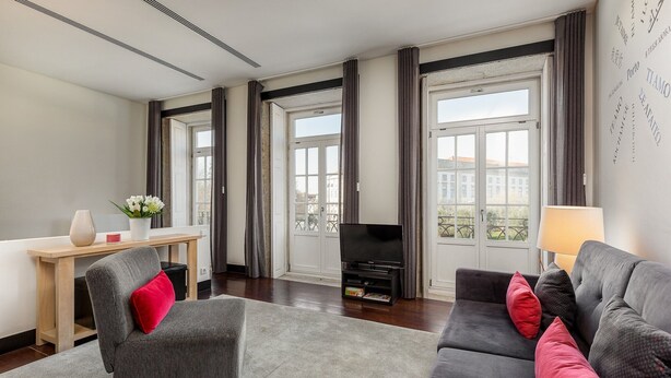 A modern living room with a sofa, armchair, and a flat-screen TV. - Charming Apartment with street-view in Porto (Oporto)