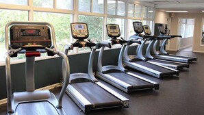 Eine Reihe von Laufbändern in einem Fitnessstudio mit großen Fenstern und Blick auf Bäume.