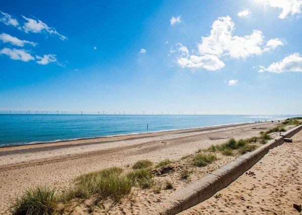 A beach with a clear sky, sandy shore, and wind turbines in the distance.