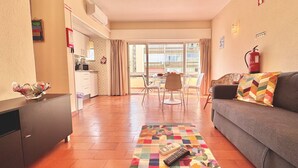 A living room with a sofa, a coffee table with a quilt, and a kitchen area with a dining table and chairs. - VILAMOURA CENTRAL 10 by HOMING (Vilamoura)