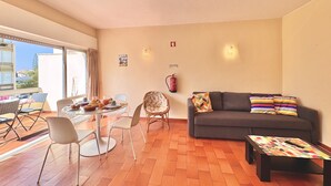 A living room with a sofa, a coffee table, and a dining area with chairs and a table. - VILAMOURA CENTRAL 10 by HOMING (Vilamoura)