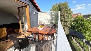 An outdoor balcony with a wooden table, wicker chairs, and a bowl of fruit.
