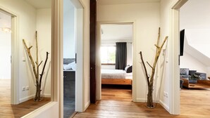 A hallway leading to a bedroom with a bed, a TV, and a sofa. There are wooden branches in vases on the floor.