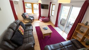 Ein Wohnzimmer mit einer Sofagarnitur, einem Couchtisch, einem roten Sitzsack und einem Holzregal mit einer Pflanze.