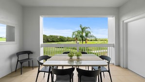 A balcony with a table and chairs, a view of a green landscape with trees and a clear sky. - Condo with Golf Course Views, Near Attractions (Kissimmee)