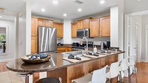 A modern kitchen with wooden cabinets, stainless steel appliances, a granite countertop, and a bar area with stools. - Condo with Golf Course Views, Near Attractions (Kissimmee)