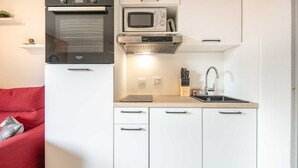 Una kitchenette compacta con horno integrado, microondas y estufa. Incluye un lavamanos con grifo, una encimera y un juego de cuchillos.