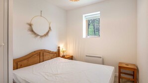 Un dormitorio con cabecera de madera, un adorno circular en la pared, una lámpara de noche y una ventana con vistas a árboles.