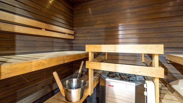 Un cuarto de sauna con bancos de madera, un balde de metal y un calentador de sauna HELO.