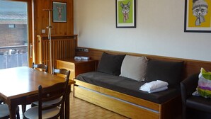 A cozy room with a wooden ceiling, a sofa with cushions, a dining table with chairs, and framed artwork on the wall.