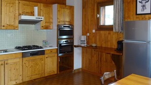 A kitchen with wooden cabinets, a gas stove, an oven, a coffee maker, and a refrigerator.
