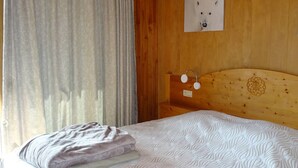 A wooden room with a bed, a wall-mounted light fixture, and a power outlet.