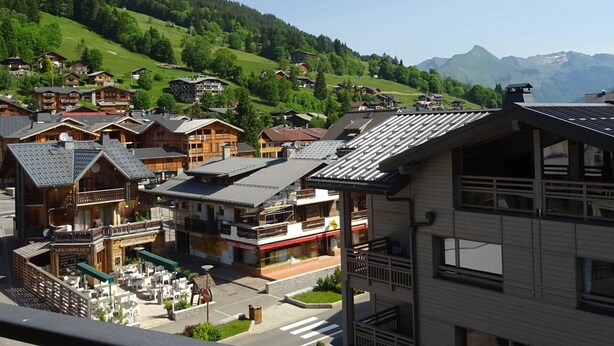A mountain village with wooden houses, a café, and a view of the surrounding hills and mountains.