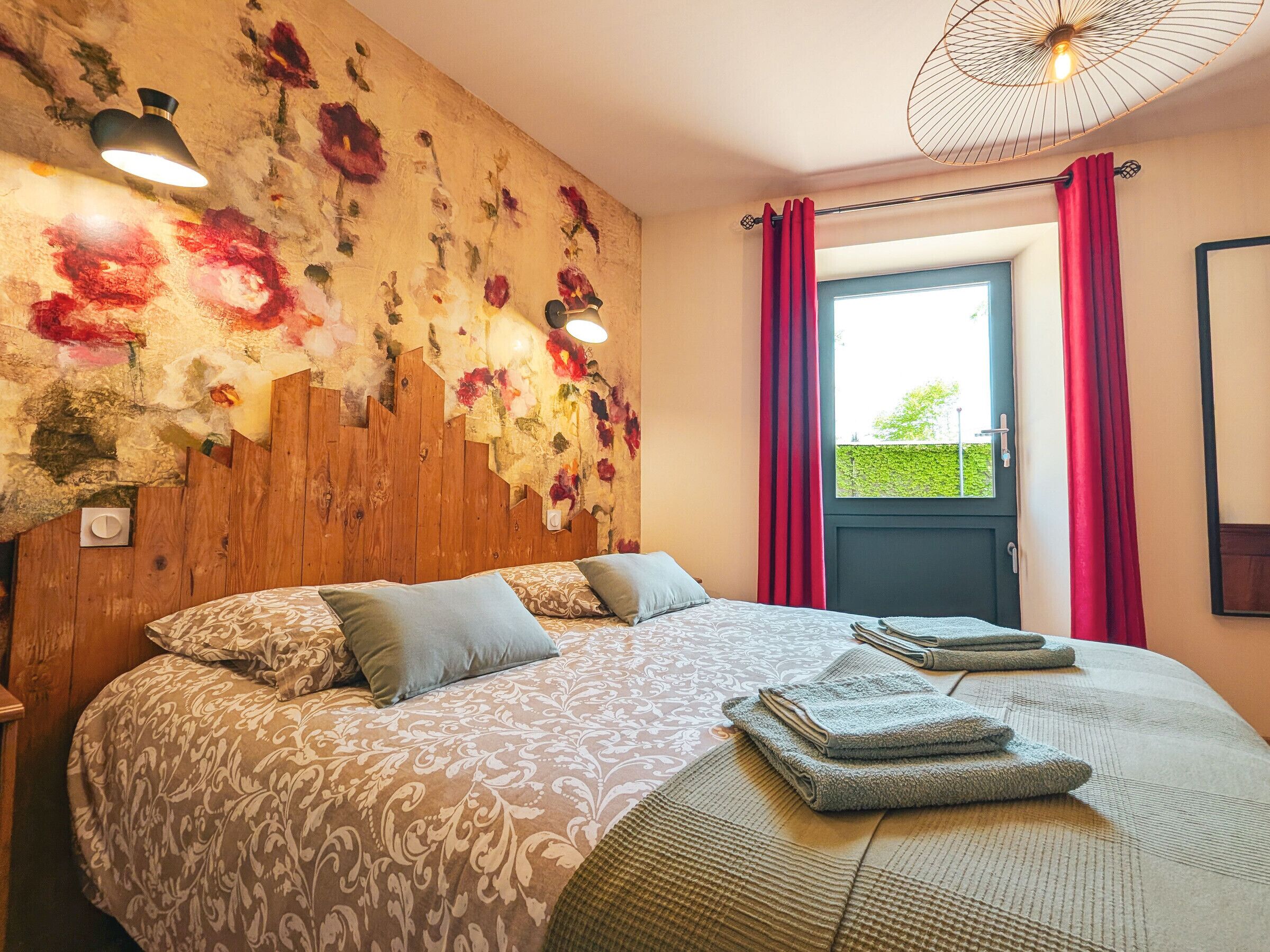 A bedroom with a bed, pillows, a wall with floral artwork, a window with curtains, and a ceiling light.