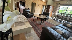 A living room with a stone fireplace, leather sofa, and a dining area with wooden chairs.