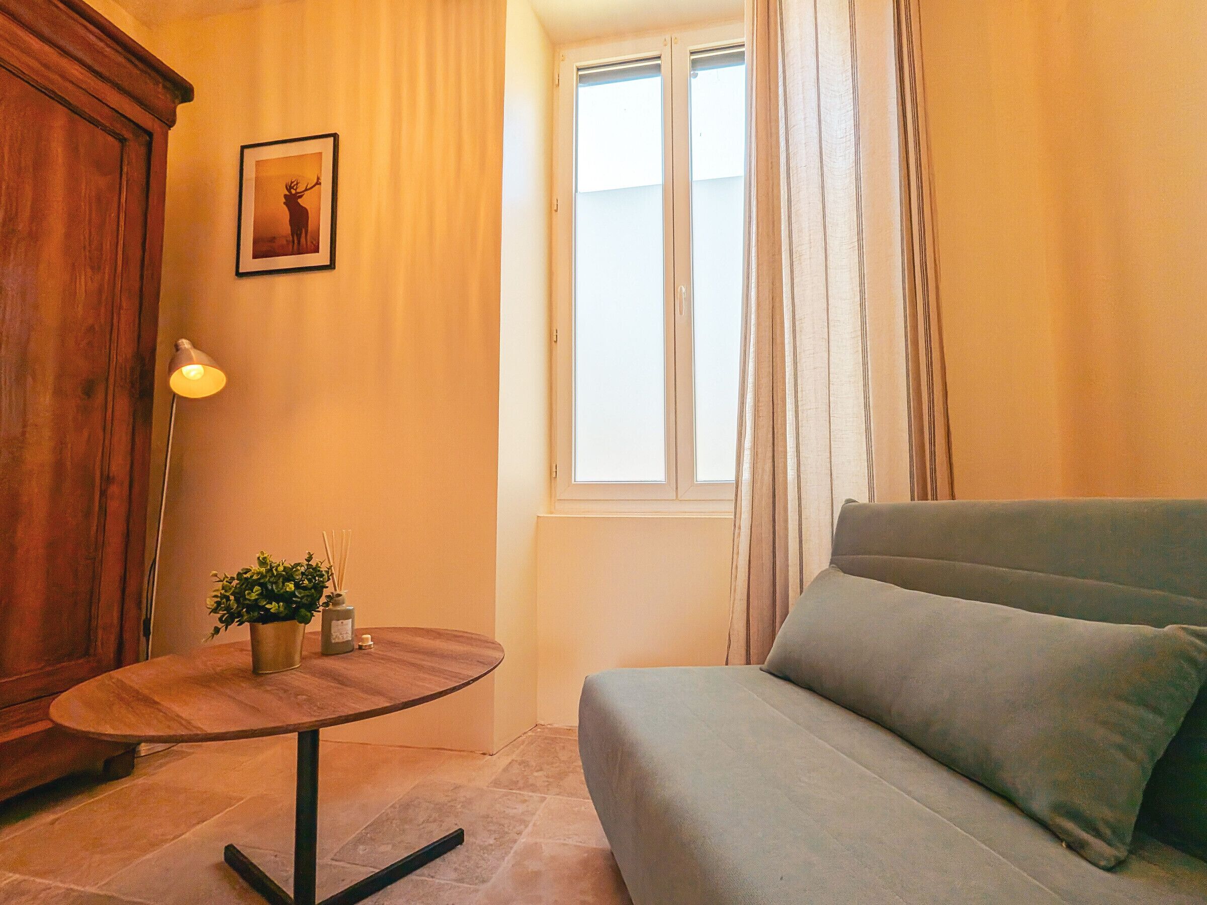 A room with a sofa, a table with a plant, a lamp, a window with curtains, and a wooden door.
